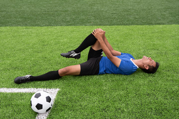 Fototapeta premium Footballer wearing a blue shirt, black pants injured in the lawn during the race.