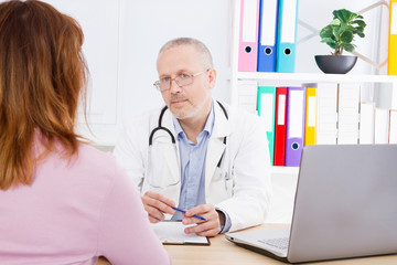 Doctor is talking with woman patient and sitting in medical office.Man in white uniform. Medical insurance. Copy space. Quality medicine concept.