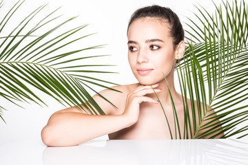 Beauty portrait. Beautiful spa woman touching her face with palms leaves isolated on white background.