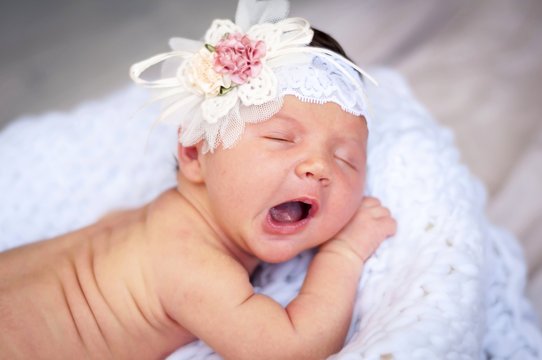Cute tiny newborn Caucasian girl yawning closeup portrait. Kid bow elastic band on her head. A two week old infant baby girl stock image.
