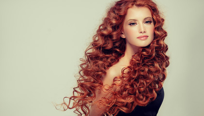 Beautiful model girl with long red curly hair .Red head . Care and beauty hair products 
