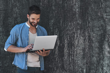 Surfing the net outdoors. Handsome young man in smart casual wear working on laptop while sitting outdoors