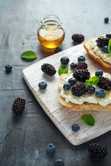 Fresh sweet Blackberry, Blueberry bruschetta, toast with cottage cheese, honey in a white board.