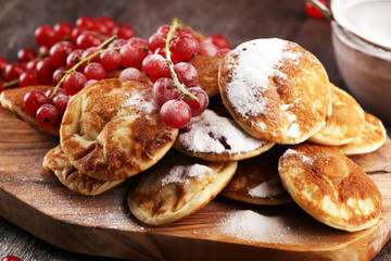 Pancakes or puffertjes with berries and maple syrup on rustic table