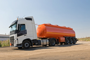 Naklejka na ściany i meble A truck with an orange tank goes on a knurled unpaved road