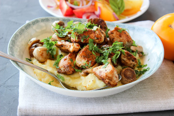 mashed potatoes with fried mushrooms and chicken on a side dish with tomatoes.