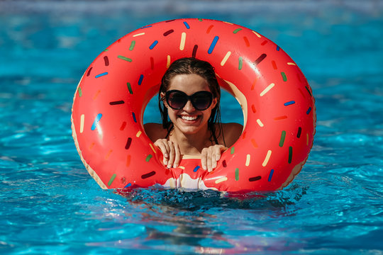 Beautiful young woman with pink donut circle have rest  in blue swimming pool
