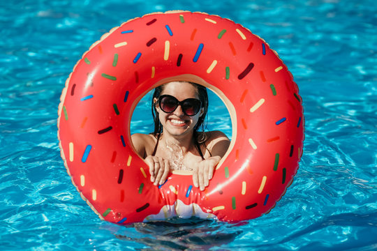 Beautiful young woman with pink donut circle have rest  in blue swimming pool
