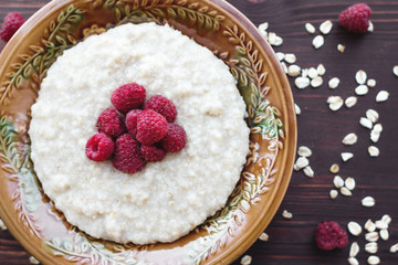 A bowl of oatmeal and raspberries on a wooden background. The concept of tasty and healthy food.
