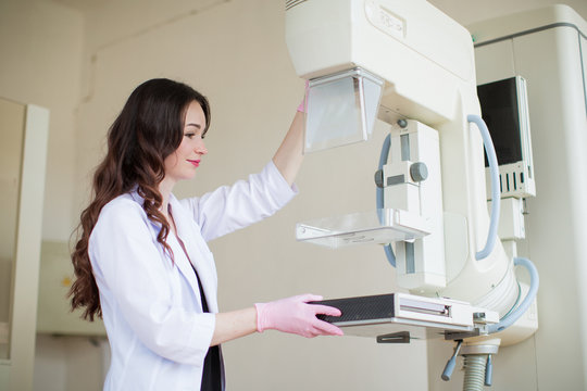 Side view of the young cheerful breast specialist standing near apparatus of the ultrasound examination of the breast in her office