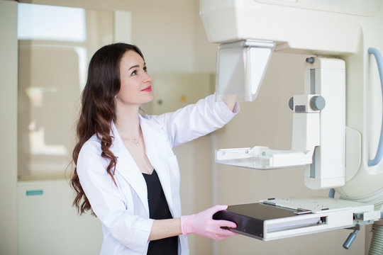 Side view of the young joyful breast specialist standing near apparatus of the ultrasound examination of the breast in her office