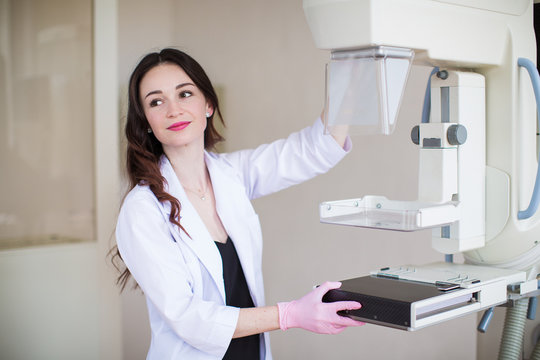 Portrait of the young happy breast specialist standing near apparatus of the ultrasound examination of the breast in her office and looking aside