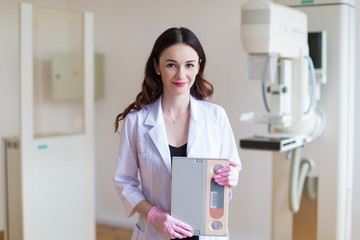 Portrait of the young smiling breast specialist in pink gloves who is standing near the apparatus of the ultrasound examination of the breast in her office