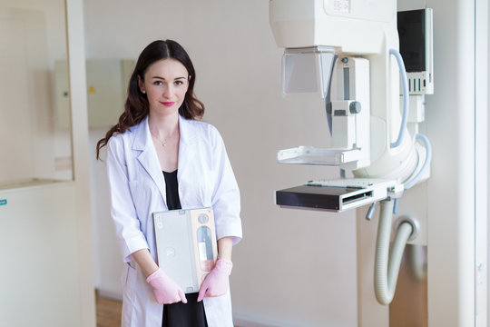 Portrait of the young breast specialist in pink gloves who is standing near the apparatus of the ultrasound examination of the breast in her office