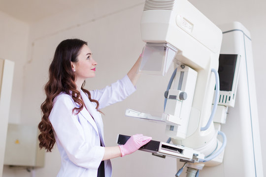 Side view of the young cheerful breast specialist in pink gloves who is preparing the apparatus of the ultrasound examination of the breast for the ultrasound examination in her office