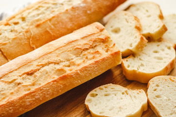 Fresh baguettes with crispy crust chopped on a cutting board on a white table. Tasty breakfast.