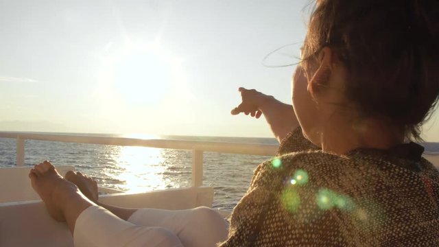 Happy young woman smiling pointing at sunrise on travel at sea. On a cruise ship vacation ferry looking at camera.