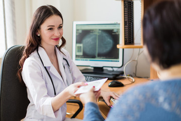 The young cheerful breast specialist sitting with the patient in her office and giving a disc with ultrasound examination