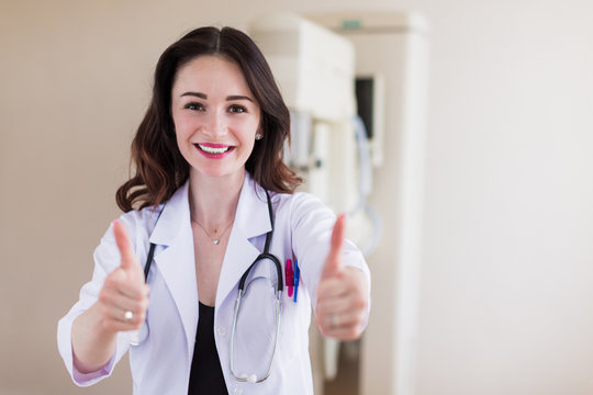 Portrait of the young beautiful breast specialist who is standing in her office and showing thumbs up and smiling