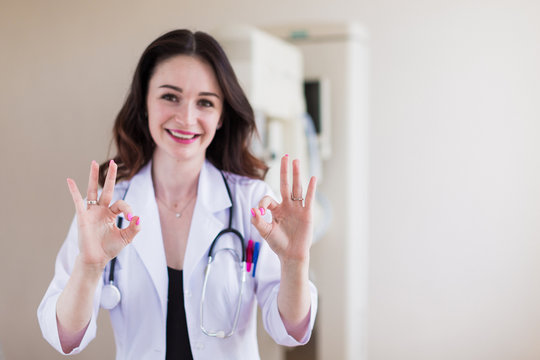 Portrait of the young beautiful breast specialist who is standing in her office and showing gesture and smiling