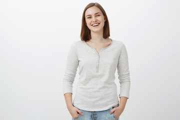 Girl feeling happy being teenager and living carefree life. Portrait of sociable friendly-looking charming female brunette holding hands in pockets casually and smiling joyfully at camera