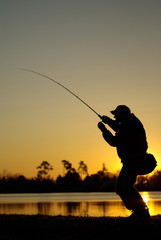 Fototapeta na wymiar Scène de pêche en eau douce sur un lac. Pêcheur au leurre combattant un poisson au soleil couchant