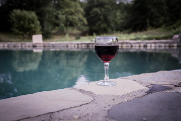 Drink in tall glass in poolside. Refreshment on summer day. Purple juice cocktail or vine. Mountain forest background.