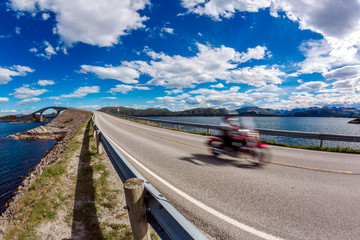 Biker rides a road with Atlantic Ocean Road in Norway.