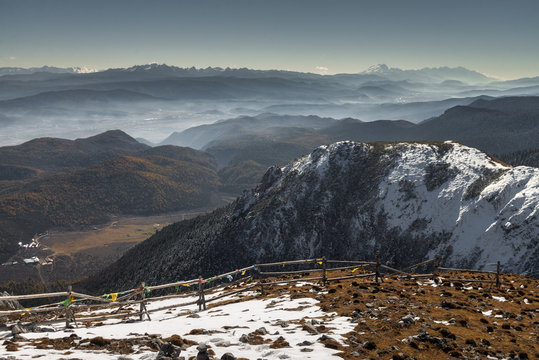 Bird eye view of foggy mountain range and pine forest with broken timber railing foreground at the peak of Shika snow mountain in Blue Moon Valley National Park, Shangri La, Yunnan, China - Powered by Adobe
