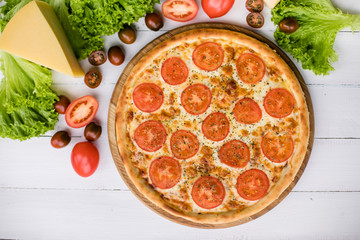 High angle view of fresh pizza on white wooden table surrounded by vegetables and cheese