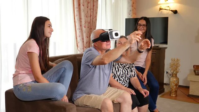 Senior man in virtual reality headset or 3d glasses having fun with his wife and granddaughters. People having fun with new technology concept. Slow motion 4k