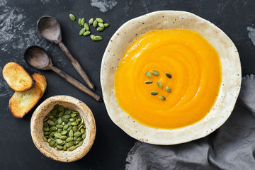 Pumpkin cream soup with toast and seeds on a rustic dark background. Top view, overhead, flat lay