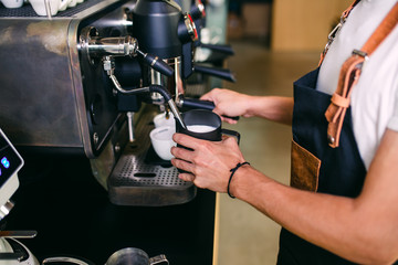 Procedure of making fresh coffee. Professional barista pouring milk into cup of espresso coffee.