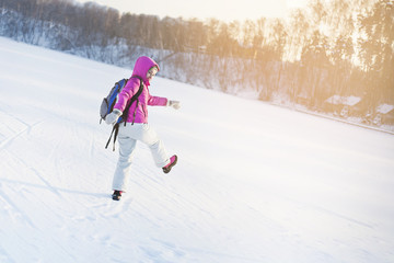 a girl in a pink jacket and a blue backpack walks through the snow on a winter day