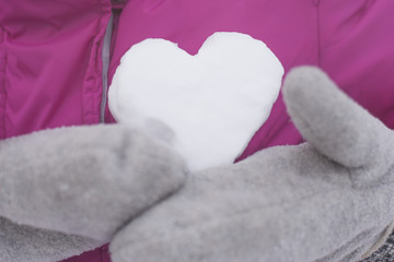 hands in mittens holding a heart made of snow