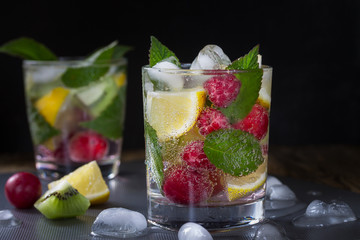 Summer refreshing carbonated drink with berries and fruits (raspberry, lemon, kiwi) and ice on a dark background. Macro