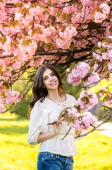 Fototapeta premium portrait of a young teenage girl looking at blooming sakura trees