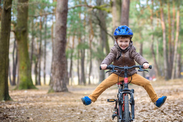 Happy kid boy of 3 or 5 years having fun in autumn forest with a bicycle on beautiful fall day....