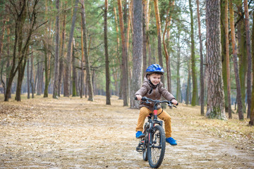 Naklejka premium Happy kid boy of 3 or 5 years having fun in autumn forest with a bicycle on beautiful fall day. Active child wearing bike helmet. Safety, sports, leisure with kids concept.
