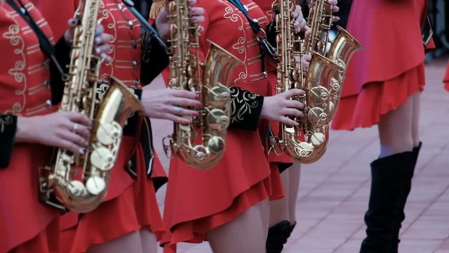 Girls in hussar red clothes and black boots play saxophones. Close-up. The brass band Kostanay.