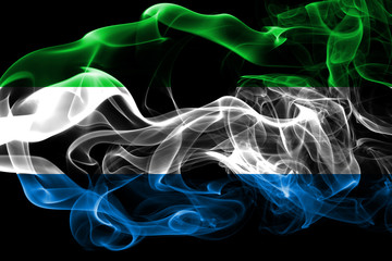 Fototapeta premium National flag of Sierra Leone made from colored smoke isolated on black background. Abstract silky wave background.