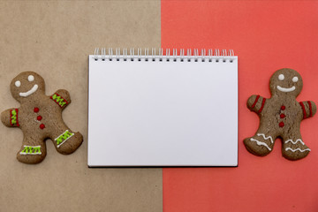 Ginger bread cookies on red and craft bown background. Blank notepad. Coffee mockup. Top view.