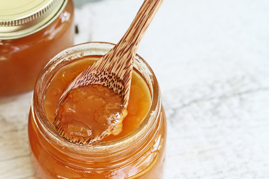 Overhead Shot Of A Wooden Spoon Full Of Homemade Cantaloupe Jam Resting In An Open Jar Filled With Jam. Could Also Be Peach Jam.