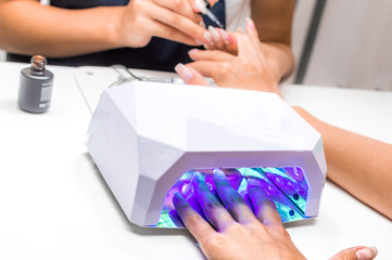 Manicure in the beauty salon. Master of manicure applies nail polish. The second hand is dried in...