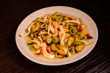 Ceramic plate with different sea food and olives on wooden table