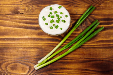 Sour cream and green onion on wooden table. Top view