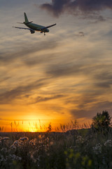 The plane flies against the sky during sunset.
