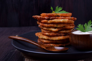 Vegetable pancakes and sour cream topped with parsley leaves on a dark plate