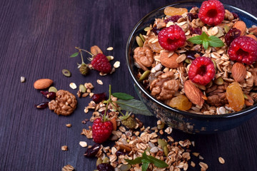 Granola made of oatmeal flakes, nuts and seeds decorated with big raspberries against the dark background