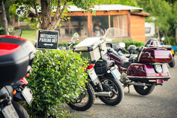 A row with parked motorcycles in a camping area with a "Motorcycle parking only" sign.